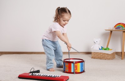 Photo of Cute little girl playing with drum, drumsticks and toy piano at home