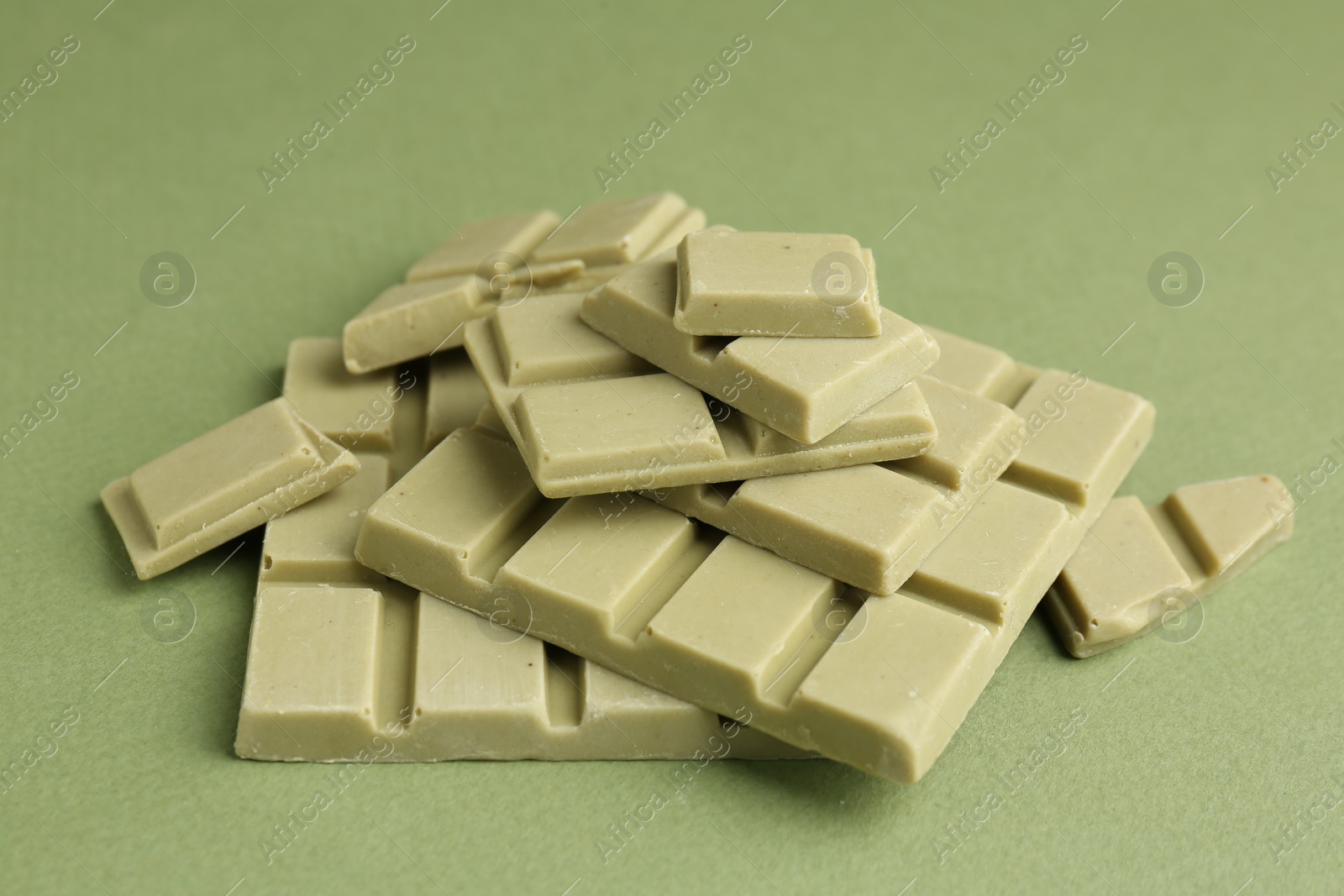 Photo of Pieces of tasty matcha chocolate bars on green background, closeup