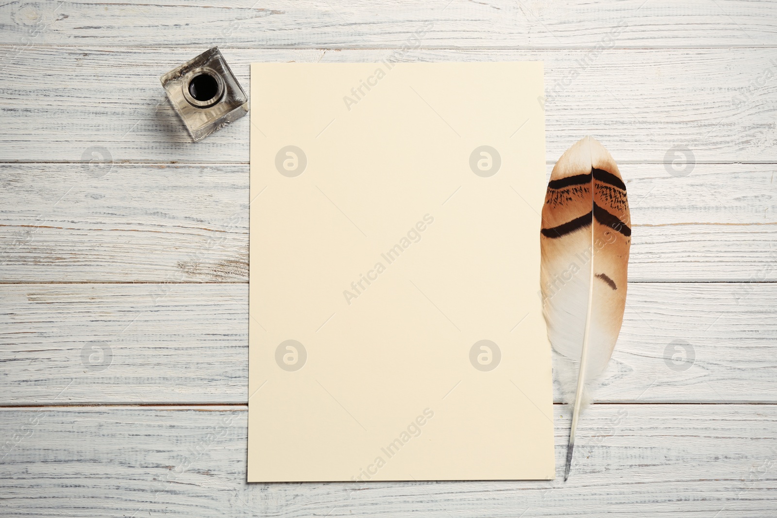 Photo of Feather pen, inkwell and blank parchment on wooden table, top view. Space for text