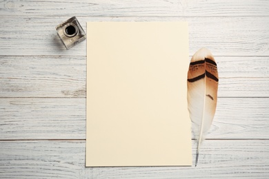 Photo of Feather pen, inkwell and blank parchment on wooden table, top view. Space for text