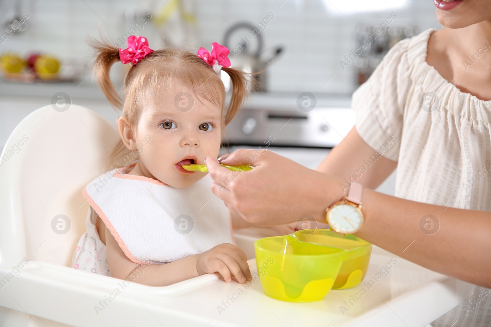 Photo of Mother feeding her little baby with healthy food in kitchen