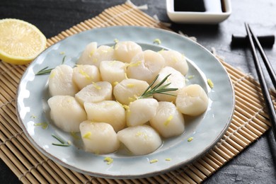 Photo of Raw scallops with lemon and rosemary on dark textured table, closeup