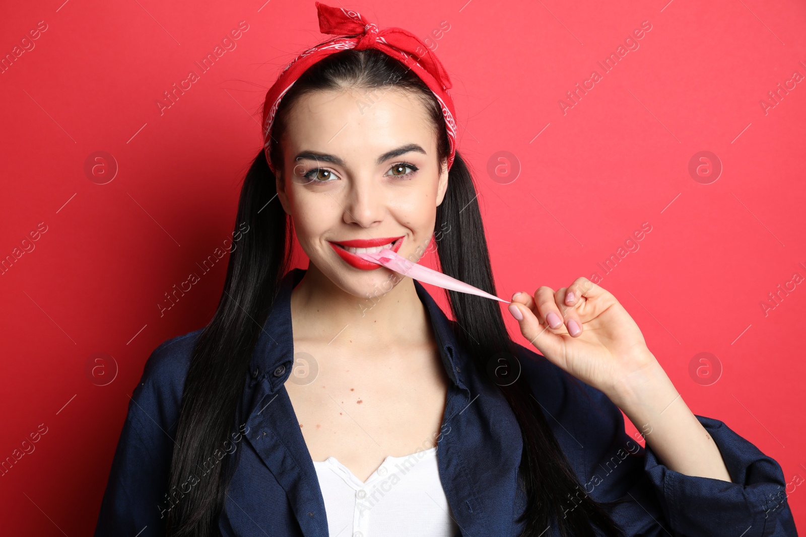 Photo of Fashionable young woman in pin up outfit chewing bubblegum on red background