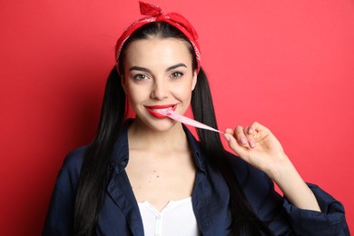 Photo of Fashionable young woman in pin up outfit chewing bubblegum on red background