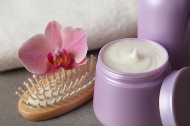 Different hair products, flower and brush on grey table, closeup