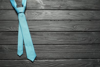 Photo of One light blue necktie on black wooden table, top view. Space for text