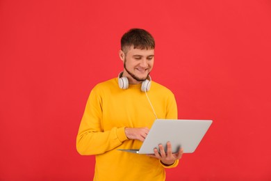 Photo of Young student with laptop and headphones on red background