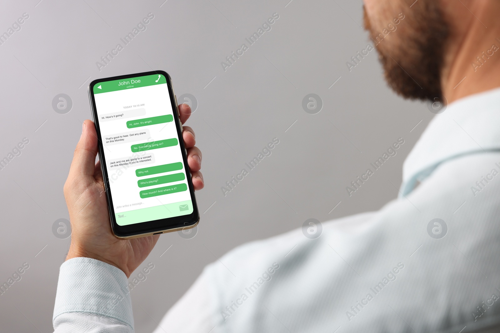 Image of Man texting with friend using messaging application on smartphone against grey background, closeup