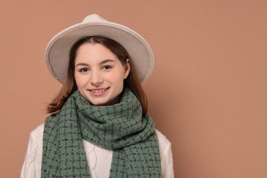 Photo of Beautiful woman in warm scarf and hat on brown background, space for text