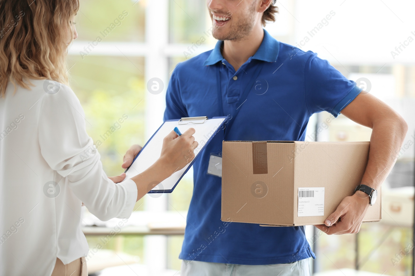 Photo of Young woman signing for delivered parcel indoors. Courier service