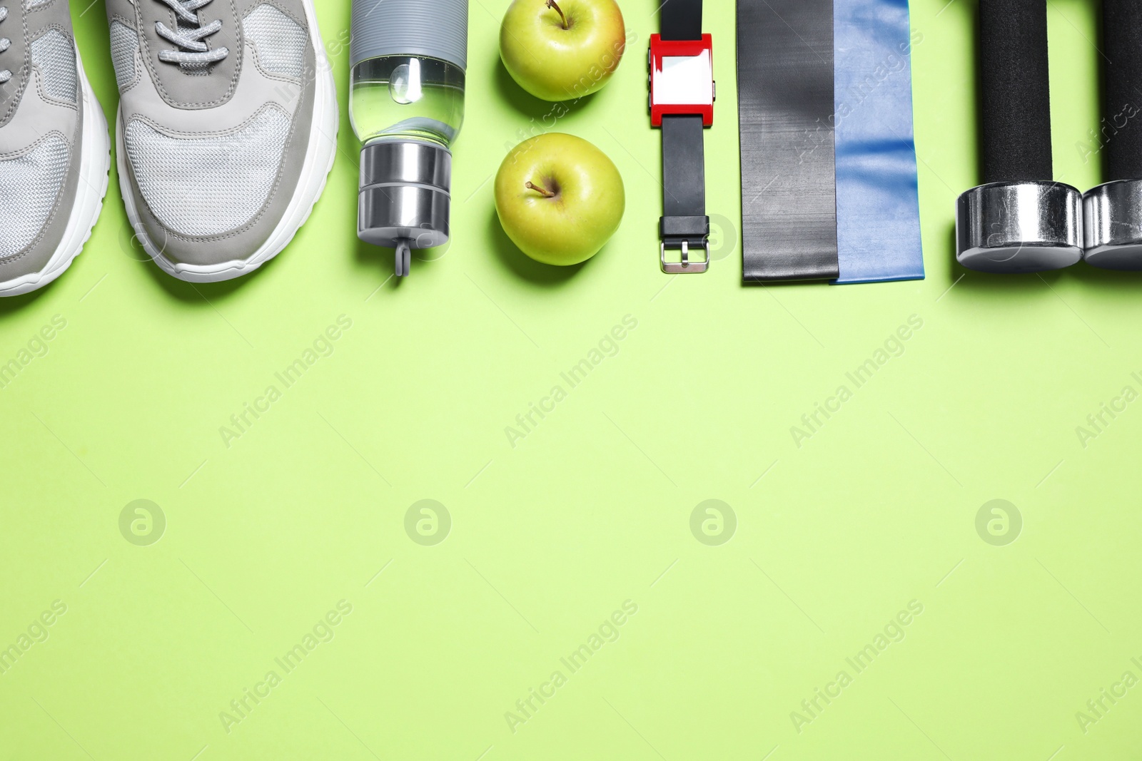 Photo of Fitness equipment, apples and water on green background, flat lay. Space for text