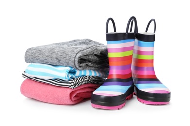 Photo of Colorful children's rubber boots and stack of clothes on white background