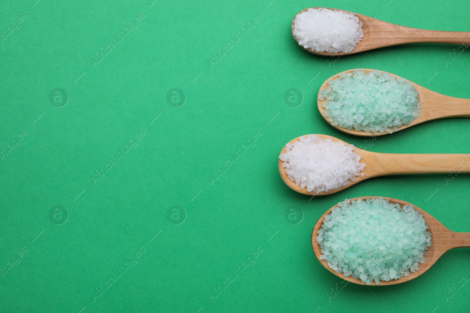 Photo of Spoons with different sea salts on green background, flat lay. Space for text