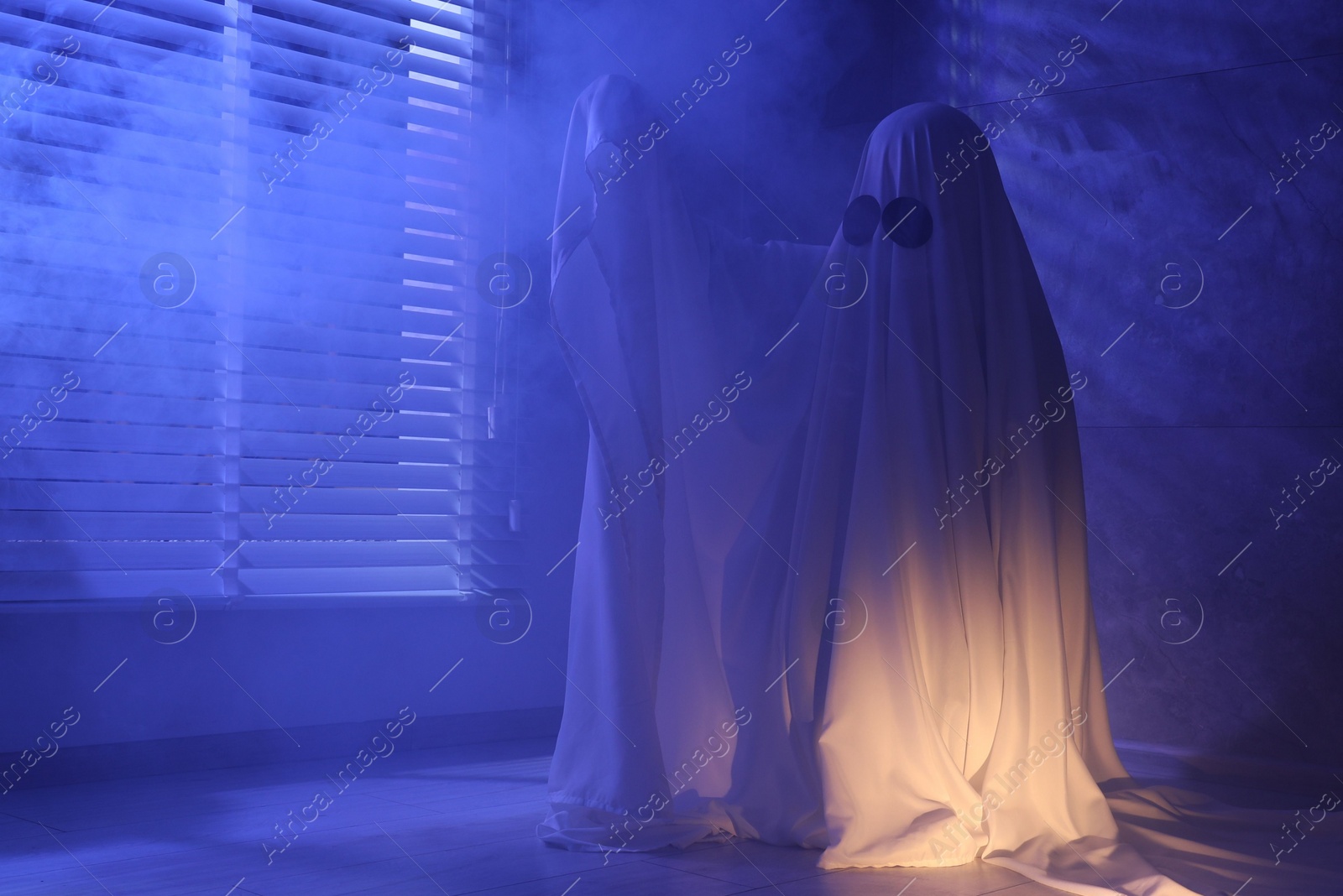 Photo of Creepy ghost. Woman covered with sheet near window in blue light