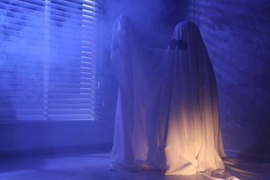 Photo of Creepy ghost. Woman covered with sheet near window in blue light