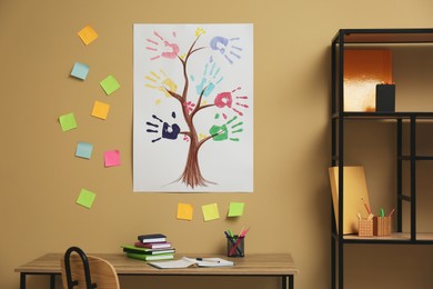 Painting with family tree of colorful palm prints on beige wall over desk in room