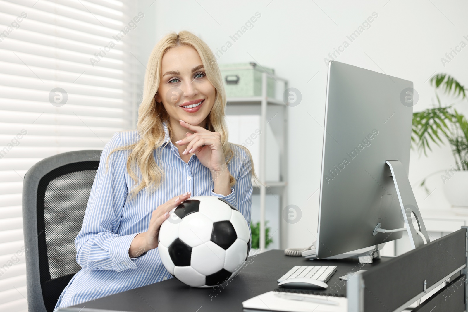 Photo of Happy woman with soccer ball at table in office