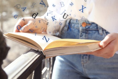 Woman reading book with letters flying over it outdoors on sunny day, closeup