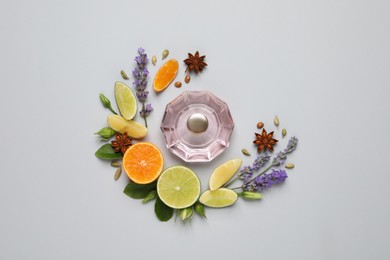 Flat lay composition with bottle of perfume, citrus  fruits and flowers on light grey background