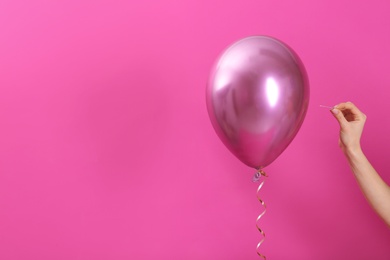 Woman piercing balloon with needle on color background, closeup. Space for text