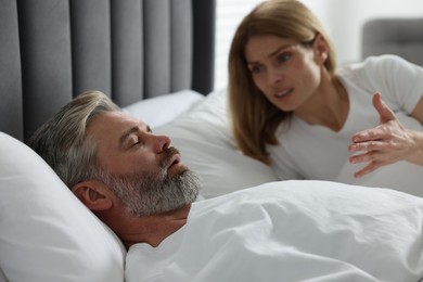 Photo of Irritated woman near her snoring husband in bed at home