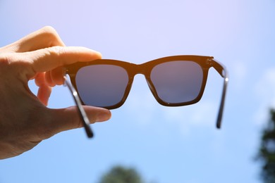 Photo of Mature man holding stylish sunglasses outdoors on sunny day, closeup