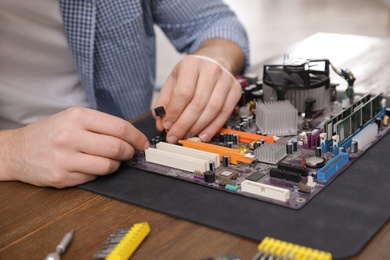 Photo of Male technician repairing motherboard at table, closeup