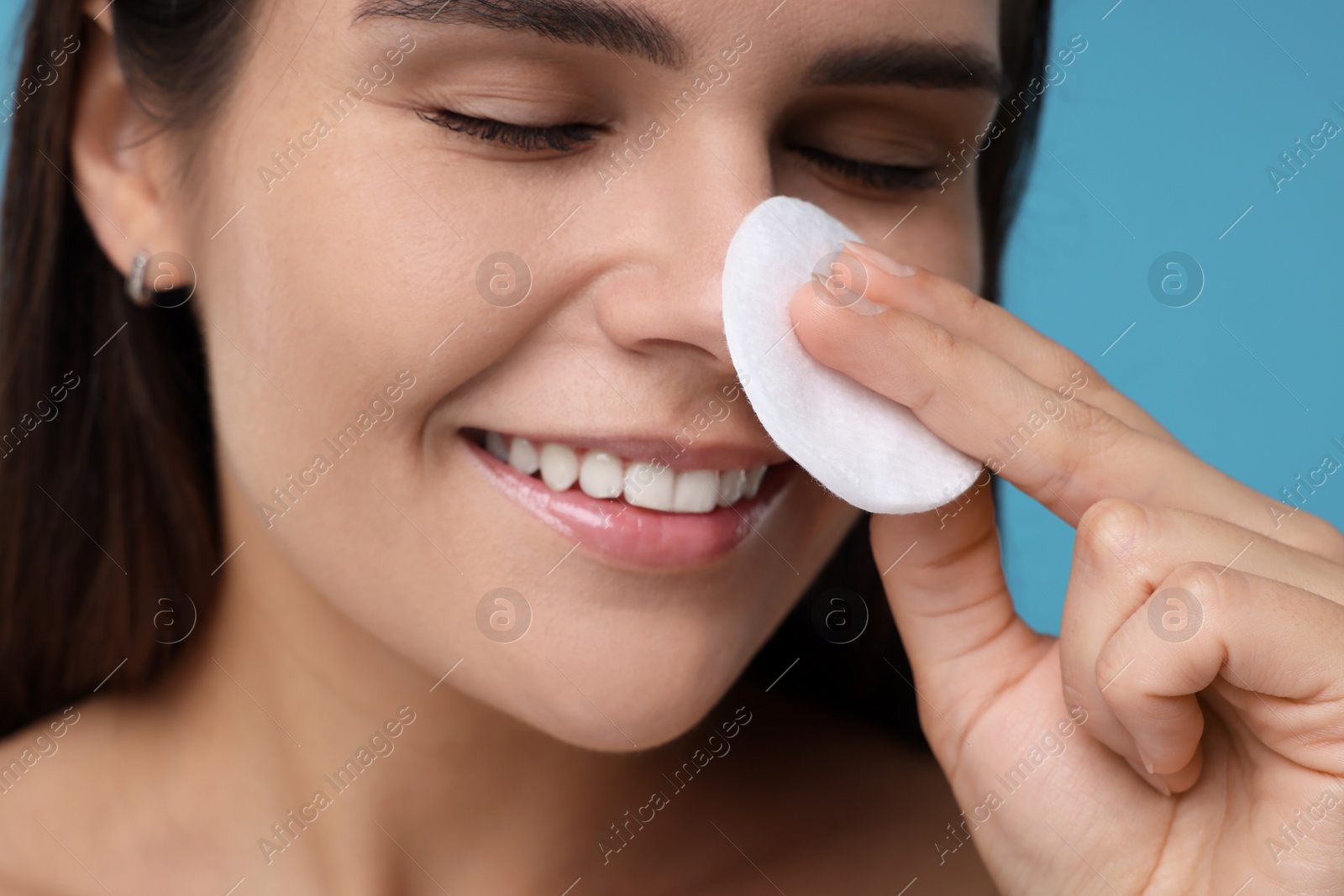 Photo of Young woman with cotton pad on light blue background, closeup