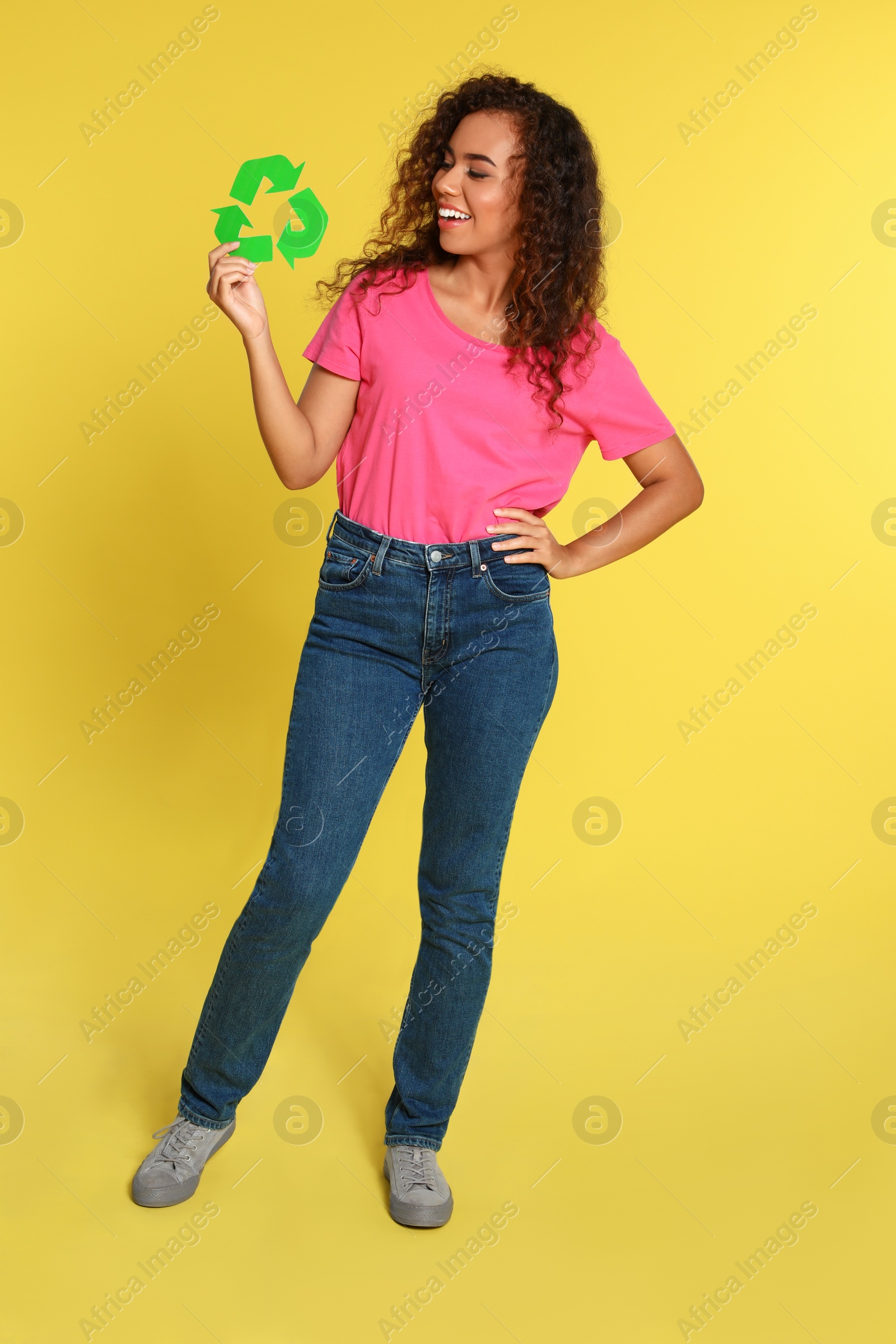 Photo of Young African-American woman with recycling symbol on yellow background