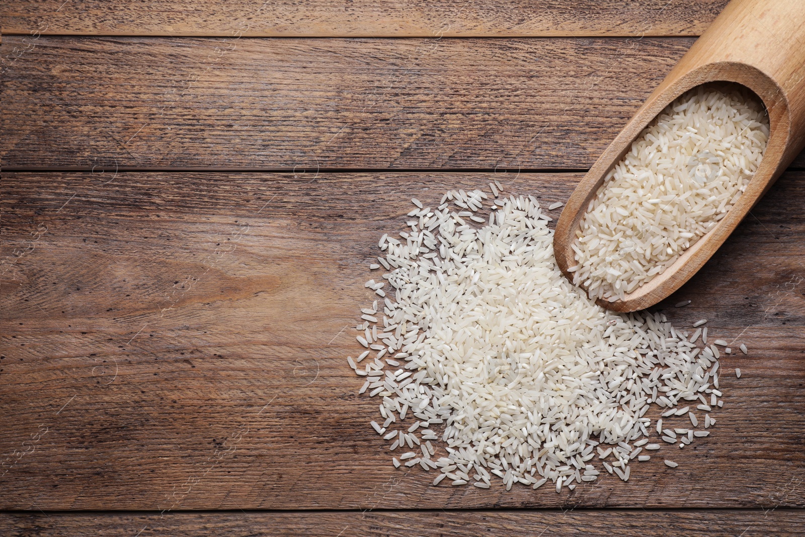 Photo of Uncooked rice and scoop on wooden table, top view. Space for text