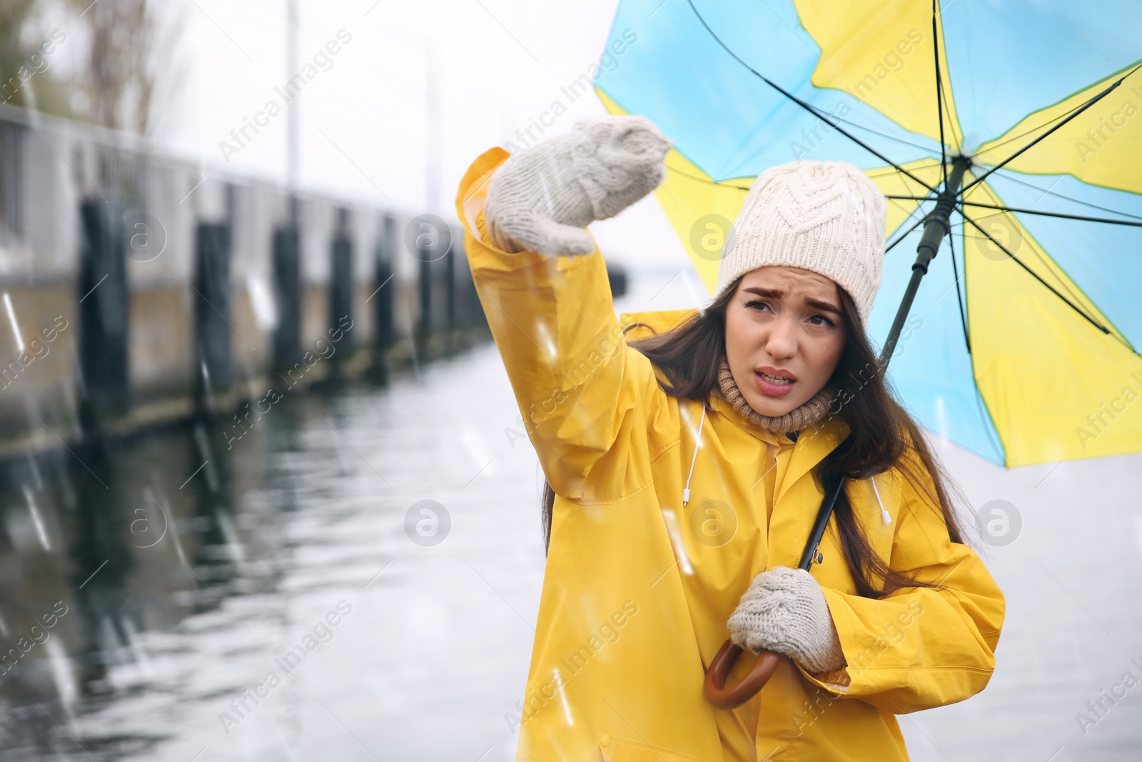 Photo of Woman in yellow raincoat with umbrella caught in gust of wind near river