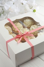 Photo of Tasty cupcakes with vanilla cream in box and orchid flowers on white wooden table, closeup