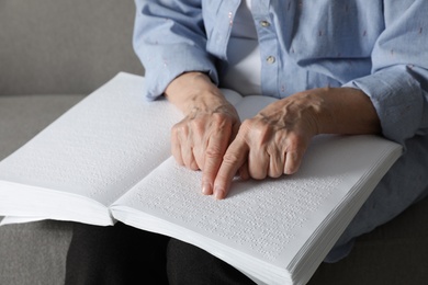 Photo of Blind senior person reading book written in Braille on sofa, closeup
