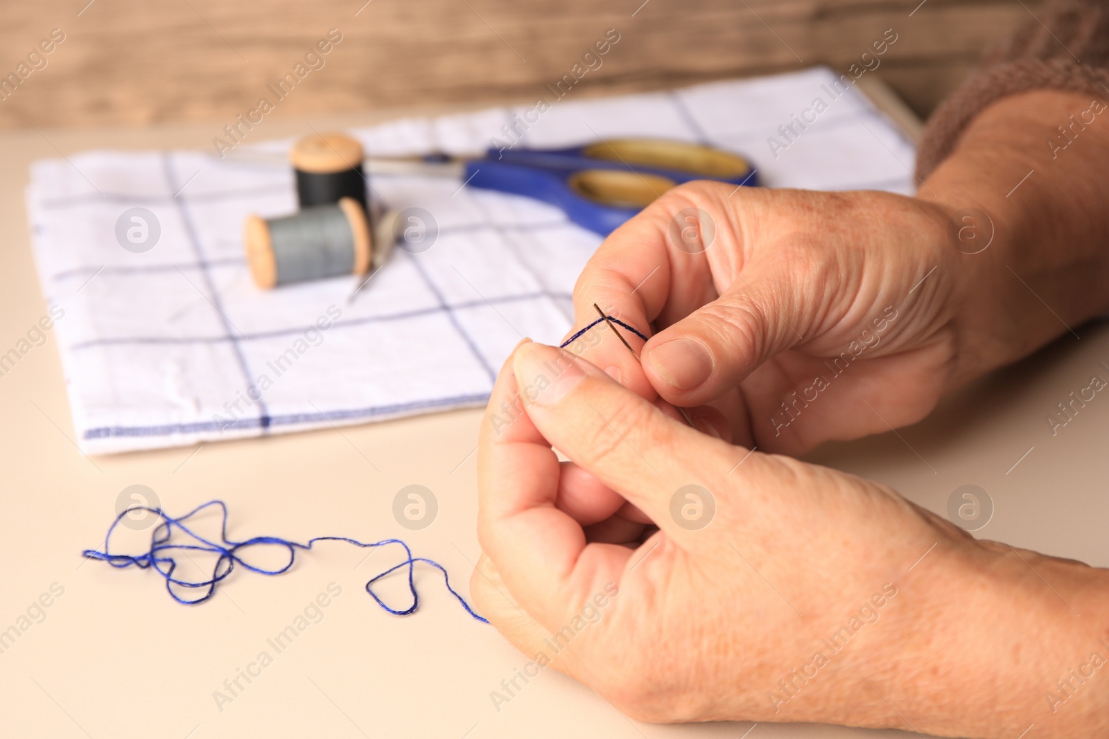 Photo of Closeup view of woman threading needle at beige table, space for text