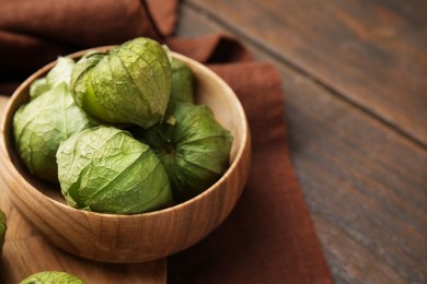 Photo of Fresh green tomatillos with husk in bowl on wooden table, closeup. Space for text