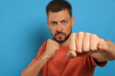Photo of Man throwing punch against light blue background, focus on fist. Space for text