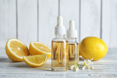 Bottles of citrus essential oil, flower and lemons on white wooden table