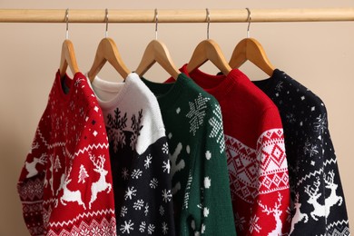 Rack with different Christmas sweaters on beige background