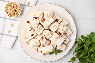 Pieces of delicious nutty nougat, peanuts and mint on white table, flat lay