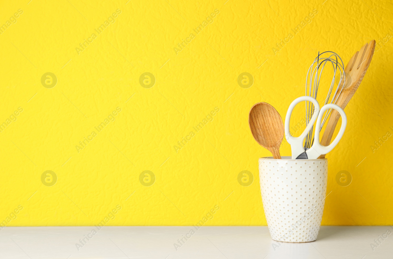 Photo of Holder with kitchen utensils on white table against yellow background. Space for text