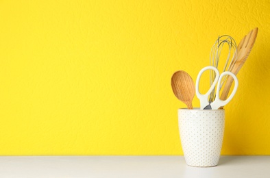 Holder with kitchen utensils on white table against yellow background. Space for text