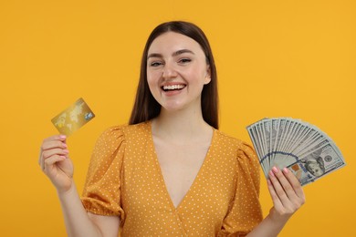 Photo of Happy woman with credit card and dollar banknotes on orange background