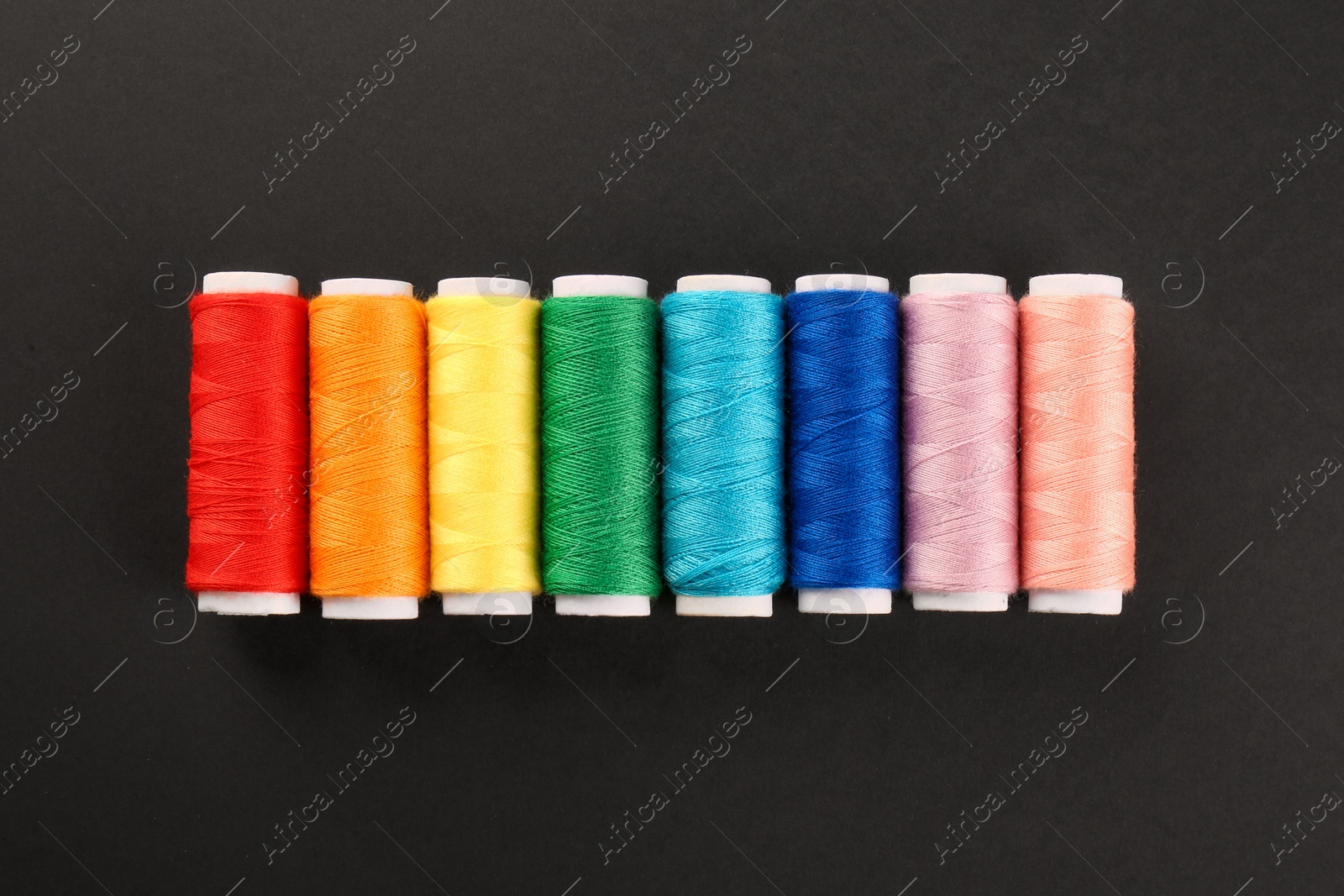 Photo of Different colorful sewing threads on black background, flat lay