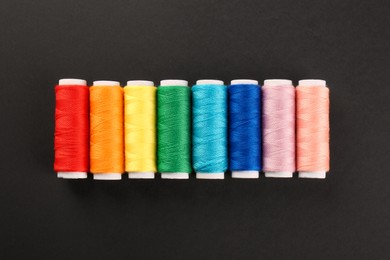 Photo of Different colorful sewing threads on black background, flat lay