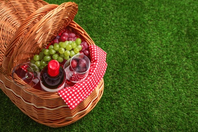 Photo of Picnic basket with wine and grapes on grass, space for text