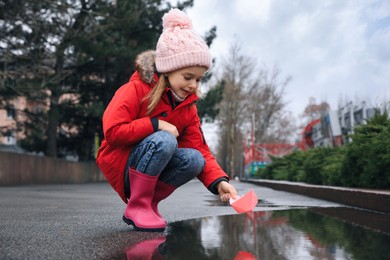 Photo of Little girl playing with paper boat near puddle outdoors