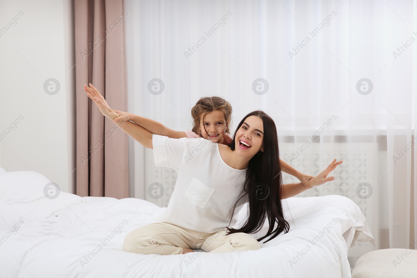 Photo of Happy woman and her daughter having fun on bed at home. Mother's day celebration