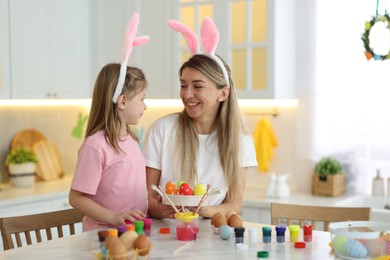 Photo of Easter celebration. Happy mother and her cute daughter with painted eggs at white marble table in kitchen