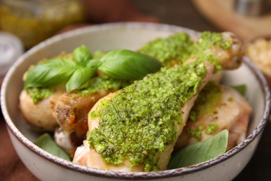 Delicious fried chicken drumsticks with pesto sauce and basil in bowl, closeup