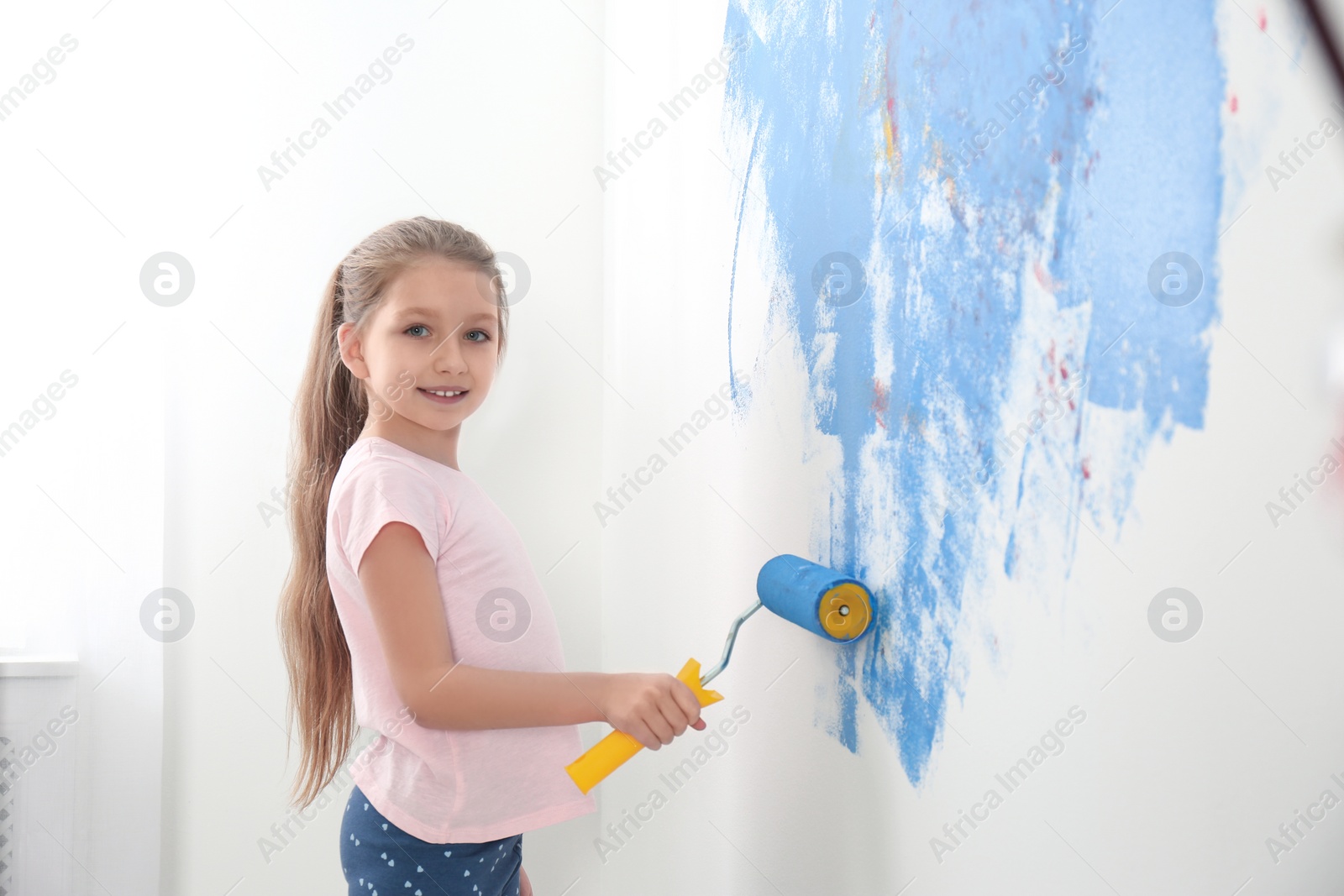 Photo of Little child painting wall with roller brush indoors